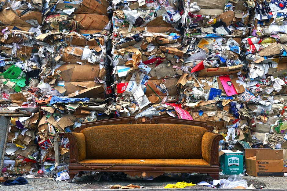 A person's hand holding a green and blue plastic shopping bag filled with household items, likely related to home relocation or packing. The bag appears to contain soft materials such as clothing or fabric, and is being held in front of a plain, light-colored background. This image illustrates the process of packing or decluttering in preparation for a move, aligning with furniture disposal or removal services offered by Putney Removals as part of house removals or moving logistics. The bag's crumpled appearance and the way it is gripped suggests careful handling during packing or transportation, emblematic of packing and loading processes involved in furniture transport or home relocations.